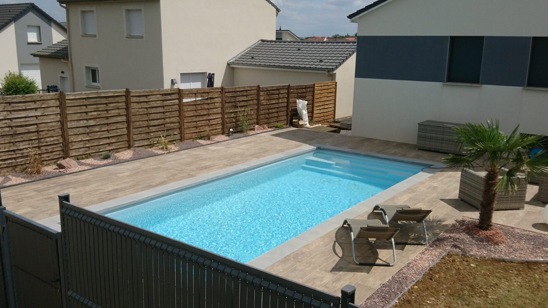 Abords de piscine avec plage, massifs de graviers et palmier